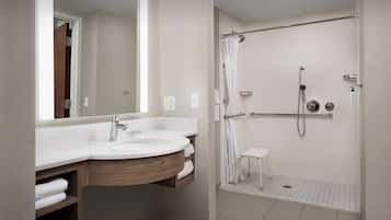 A modern bathroom with a double sink, a shower with a glass door, and a small white stool.