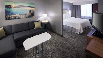 Una camera d'albergo con un divano, un tavolino, un letto, una TV e un quadro appeso al muro.