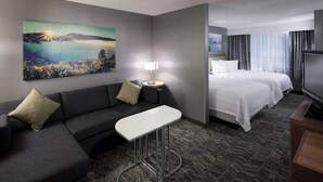 A hotel room with a gray sofa, a small white table, a bed with white bedding, a TV, and a painting of a landscape on the wall. - SpringHill Suites by Marriott Boise ParkCenter (Boise)