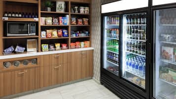 Une petite cuisine équipée d’un four à micro-ondes, d’étagères remplies d’en-cas et d’un réfrigérateur contenant des boissons.