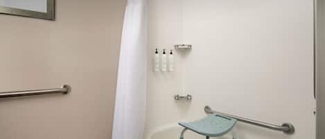 A bathroom with a bathtub, a shower curtain, a handrail, a grab bar, and a small shelf with toiletries.