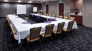 A conference room with a long table, chairs, a projector screen, and a coffee station.