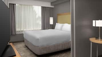 A hotel room with a large bed, a flat-screen TV, a bedside table with a lamp, and a window with curtains.
