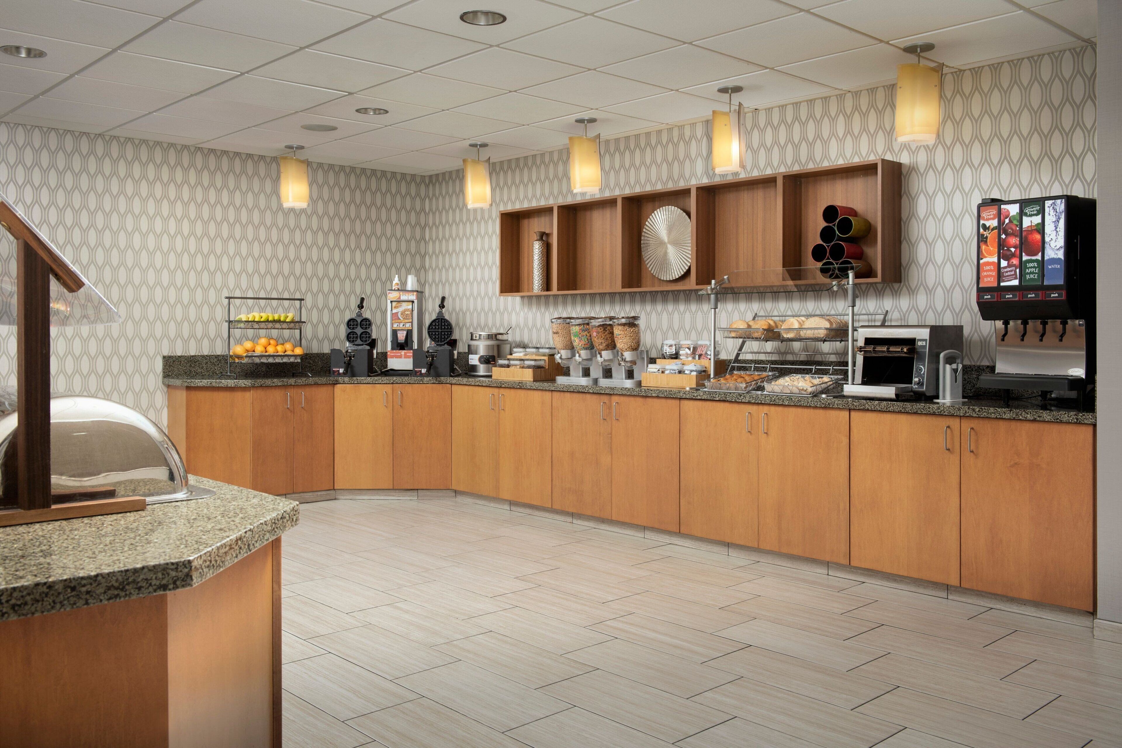 Een moderne keuken met granieten aanrechtbladen, houten kasten, een inbouw koffiehoek en een bedieningsautomaat voor drankjes.