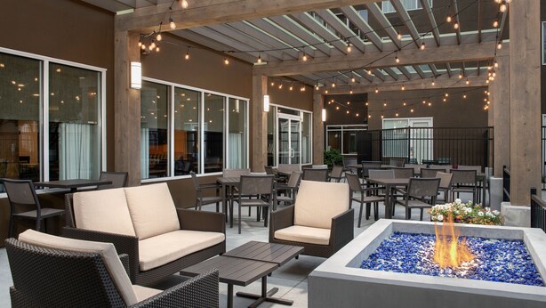 An outdoor seating area with wicker furniture, a fire feature, and string lights. - SpringHill Suites by Marriott Boise ParkCenter (Boise)