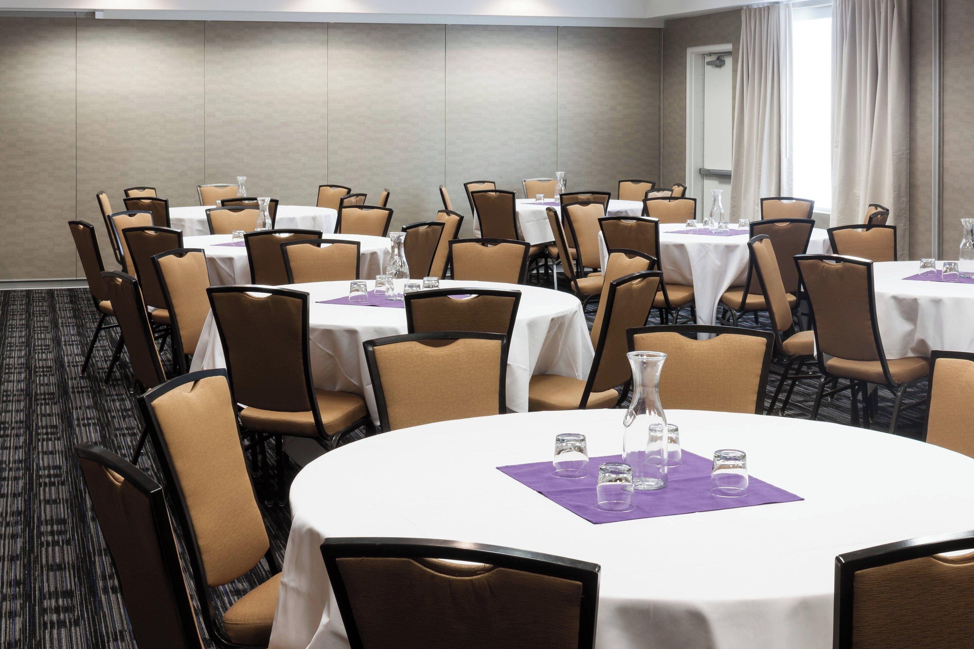 Un salón de conferencias con mesas redondas, sillas y suelo alfombrado.