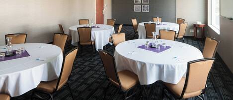 Una sala de conferencias con mesas redondas, sillas y piso alfombrado.