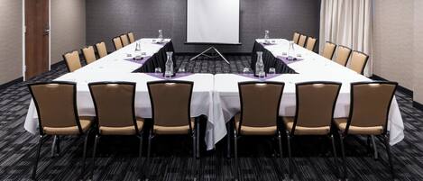 A conference room with a long table, chairs, a projector screen, and a carpeted floor.