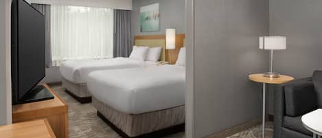 Een hotelkamer met twee bedden, een televisie, een bureau, een lamp en een bank.