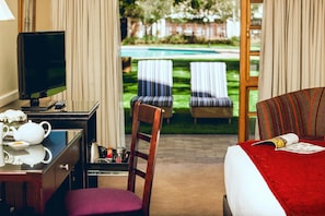 Habitación de hotel con cama, escritorio con televisor, silla y vista a una piscina y sillas de jardín.