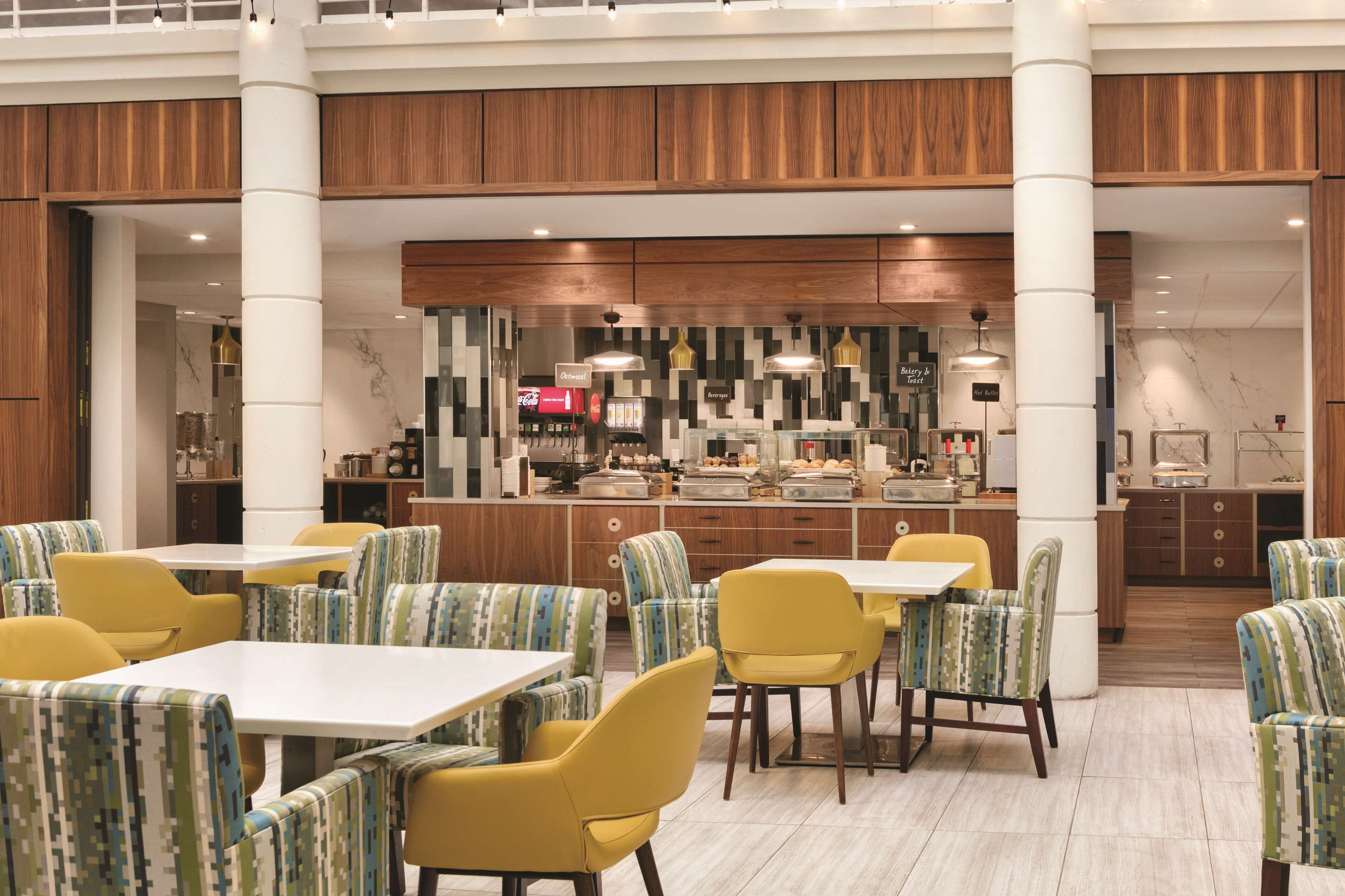 A modern dining area with yellow and green striped chairs, white tables, and a central counter with a variety of food items.