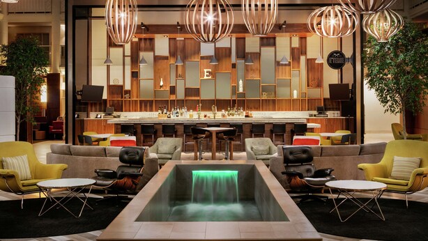 A modern bar area with a bar counter, seating, and a unique green-lit water feature. - Embassy Suites by Hilton Richmond (Richmond)