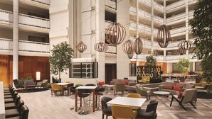 A spacious indoor area with multiple dining tables and chairs, a central seating area with sofas, and a high ceiling with hanging spherical light fixtures. - Embassy Suites by Hilton Richmond (Richmond)