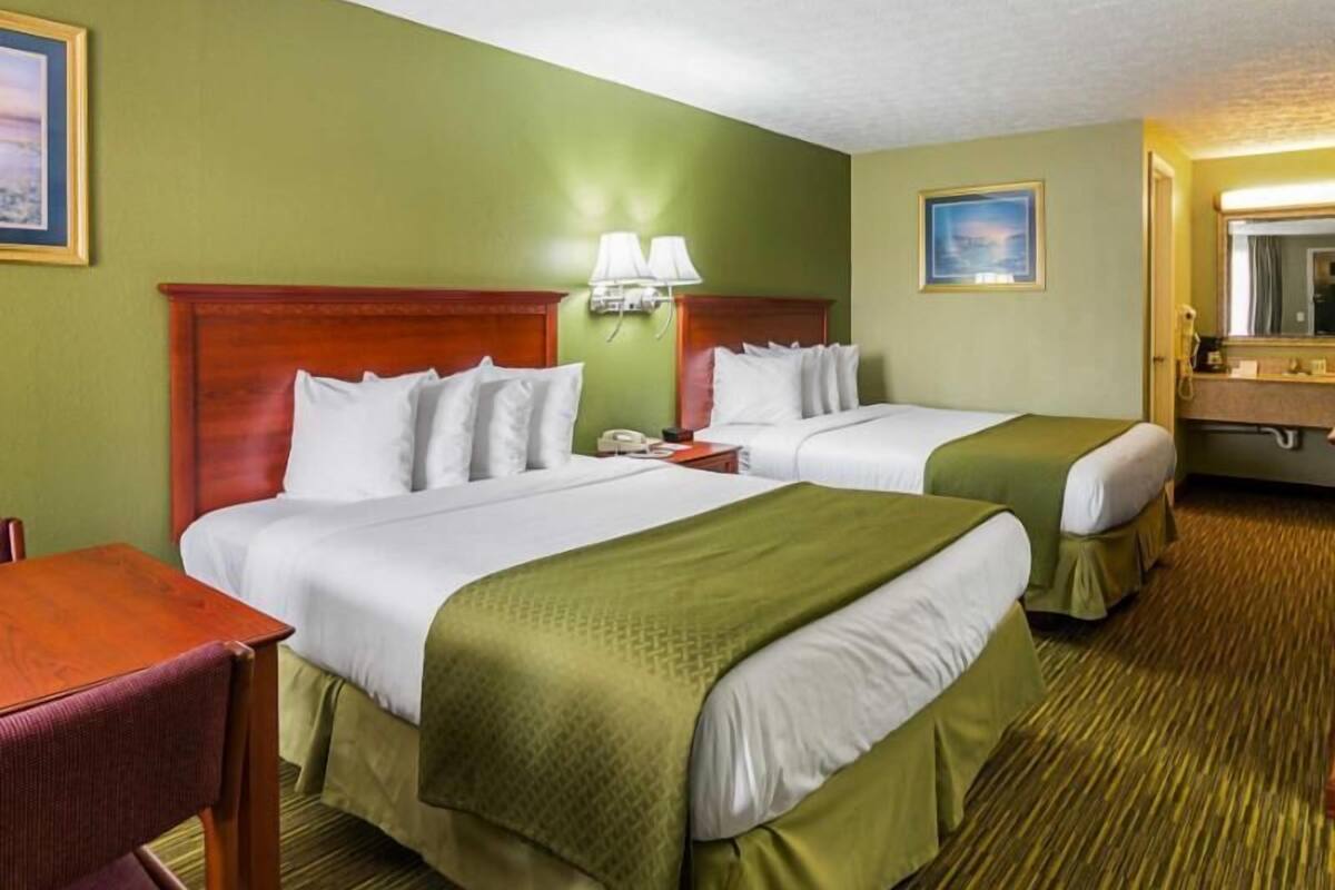 A hotel room with two beds, a desk, a chair, a lamp, and a painting on the wall.