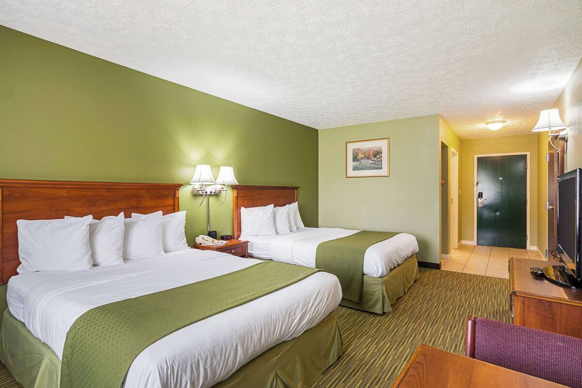 A hotel room with two beds, a desk, a chair, a TV, and a door.