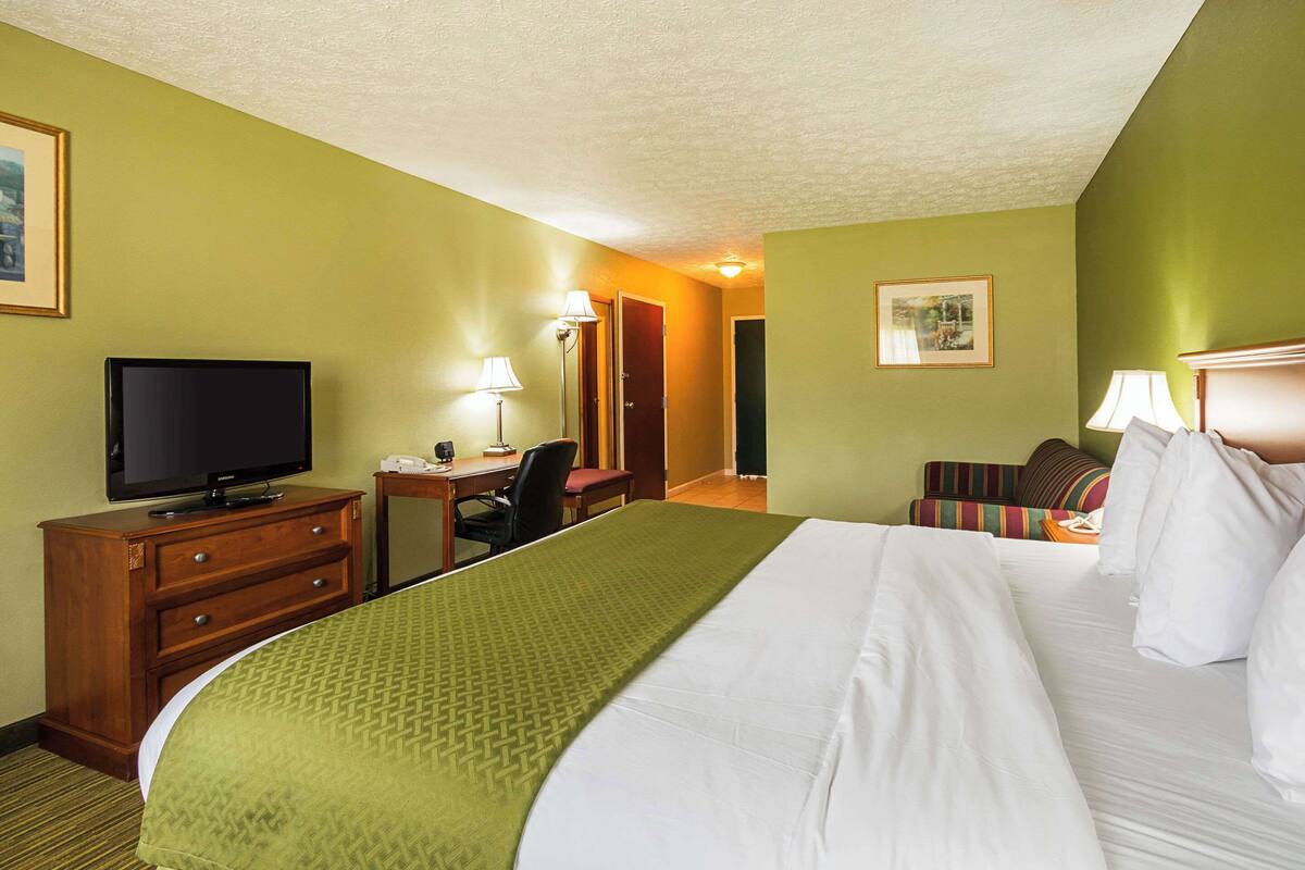 A hotel room with a large bed, a desk with a chair, a television, and a lamp.