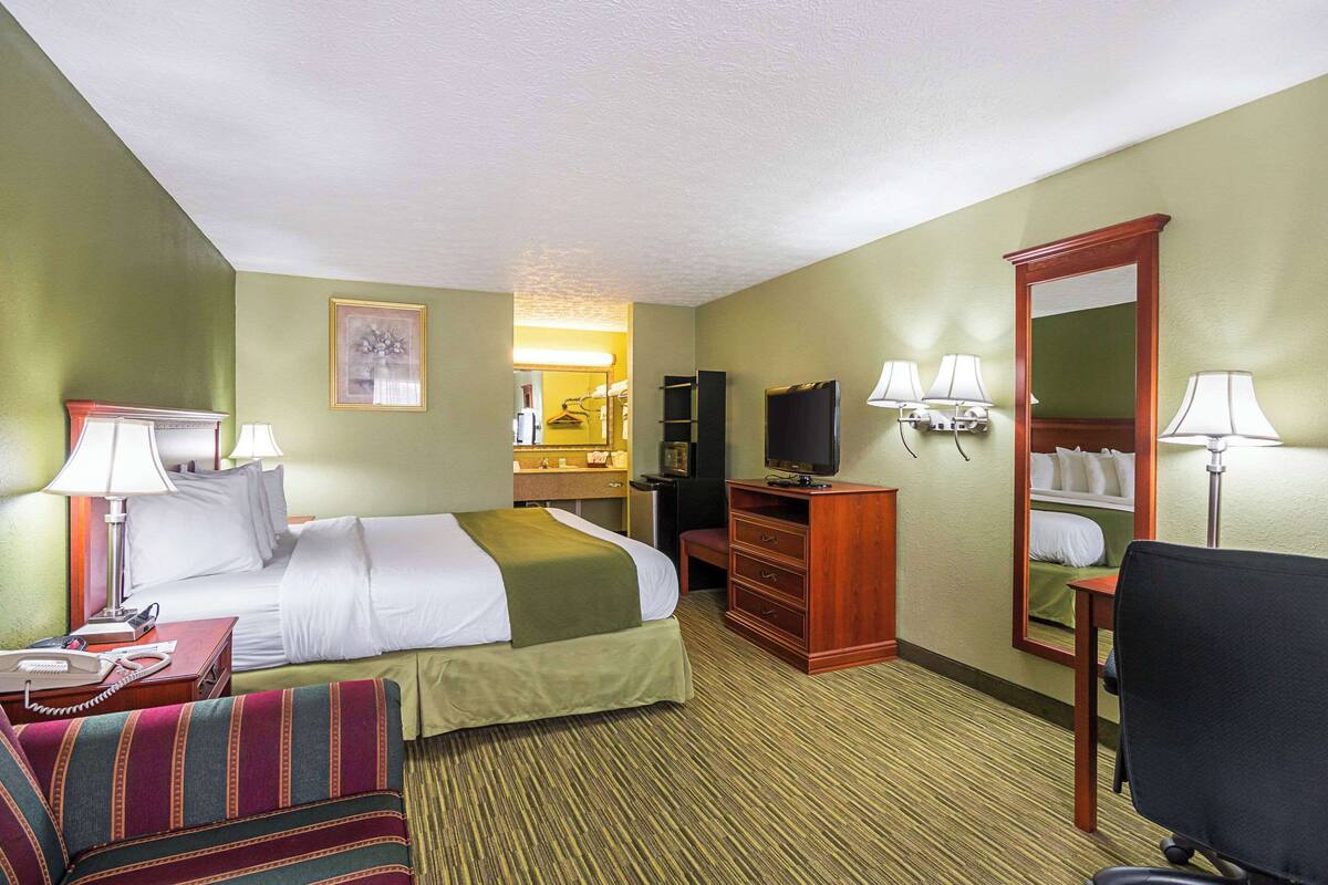 A hotel room with a bed, a desk, a chair, a TV, and a mirror.
