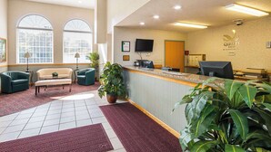 Un espace d’accueil d’hôtel comprenant un comptoir de réception, deux fauteuils, un banc et des plantes en pot.