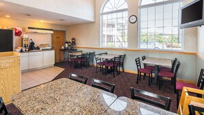 Un restaurant doté d’un espace cuisine, de tables, de chaises et de grandes fenêtres équipées de stores.