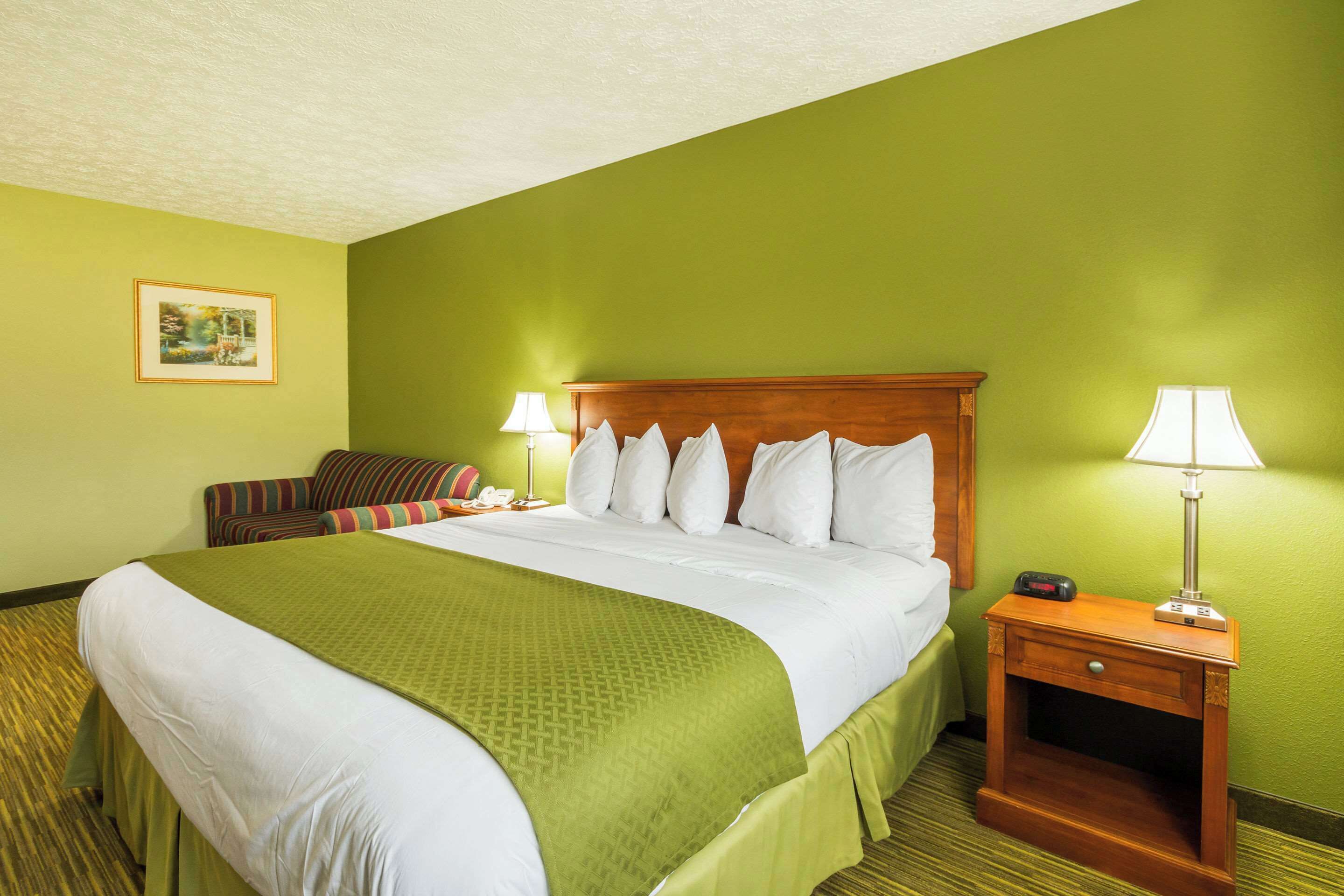 Une chambre d’hôtel avec un grand lit, une table de chevet avec une lampe, une chaise et un tableau au mur.