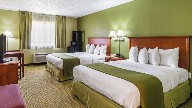 Une chambre d’hôtel avec deux lits, un bureau, une chaise, une lampe et une armoire.