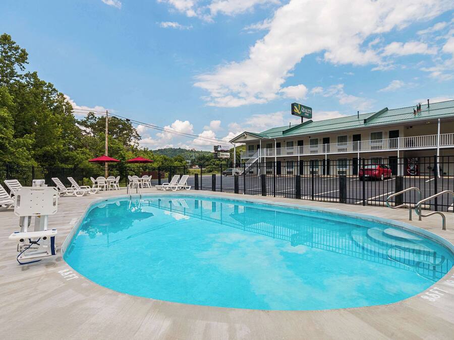 Uma piscina com espreguiçadeiras e um edifício com telhado verde ao fundo.