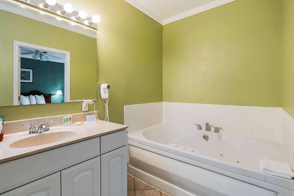 A bathroom with a large bathtub, a sink, and a vanity. There is a ceiling fan above the mirror and a hairdryer on the counter.