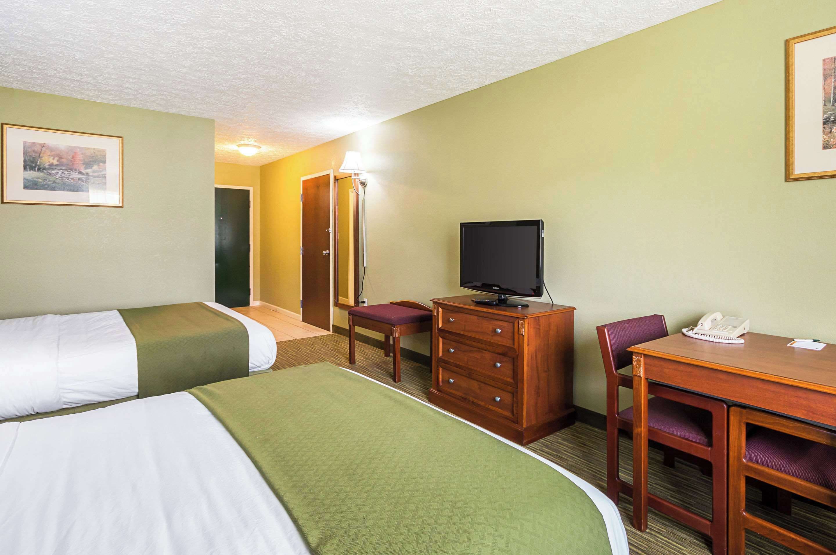 A hotel room with two beds, a desk with a telephone, a television, and a mirror.