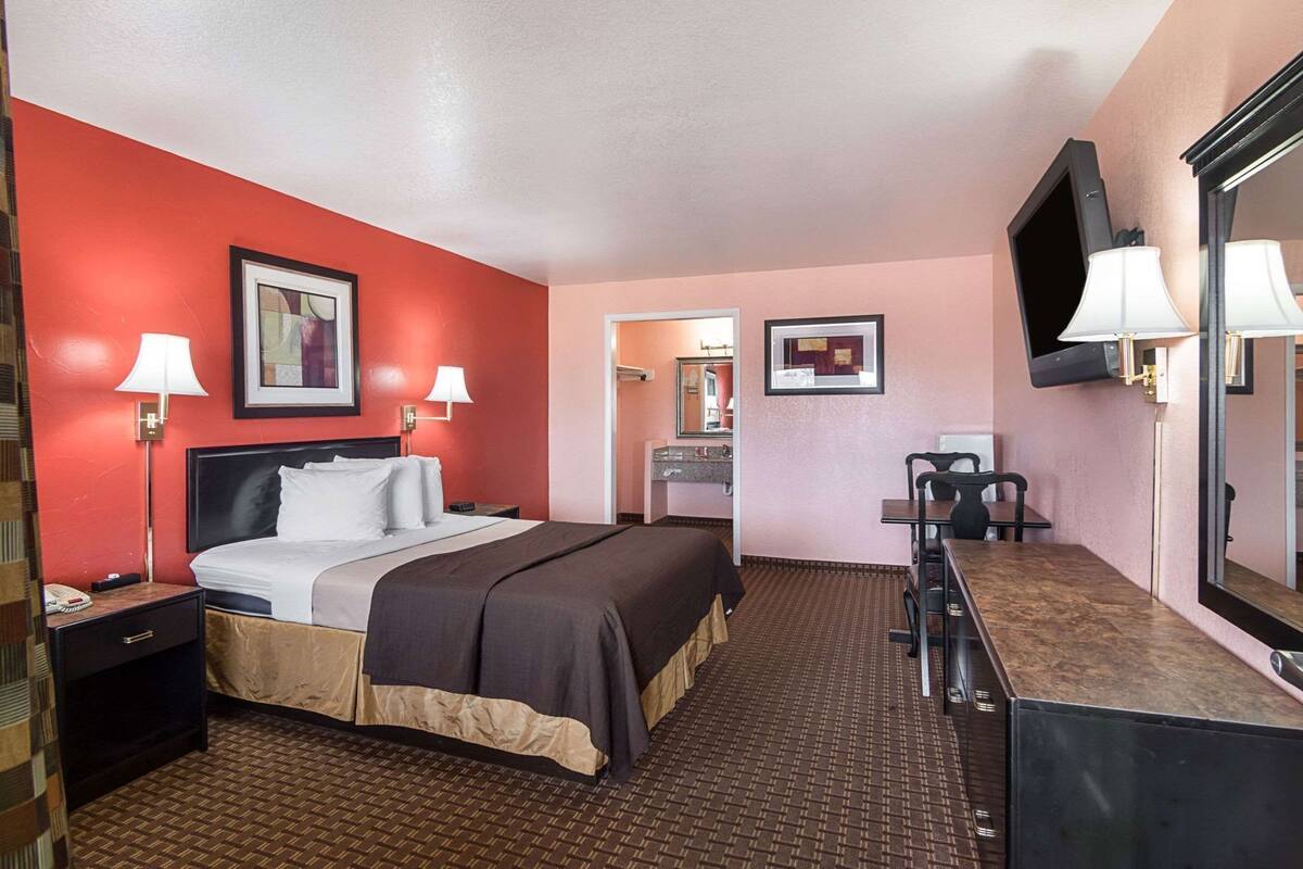 A hotel room with a bed, bedside lamps, a desk, a chair, a mirror, and a television.