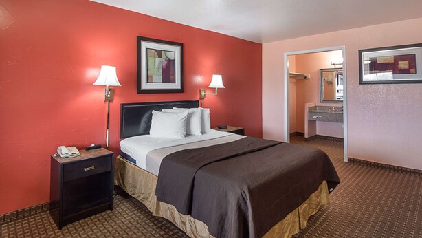 A hotel room with a bed, two bedside tables, a nightstand, a mirror, and a red wall.