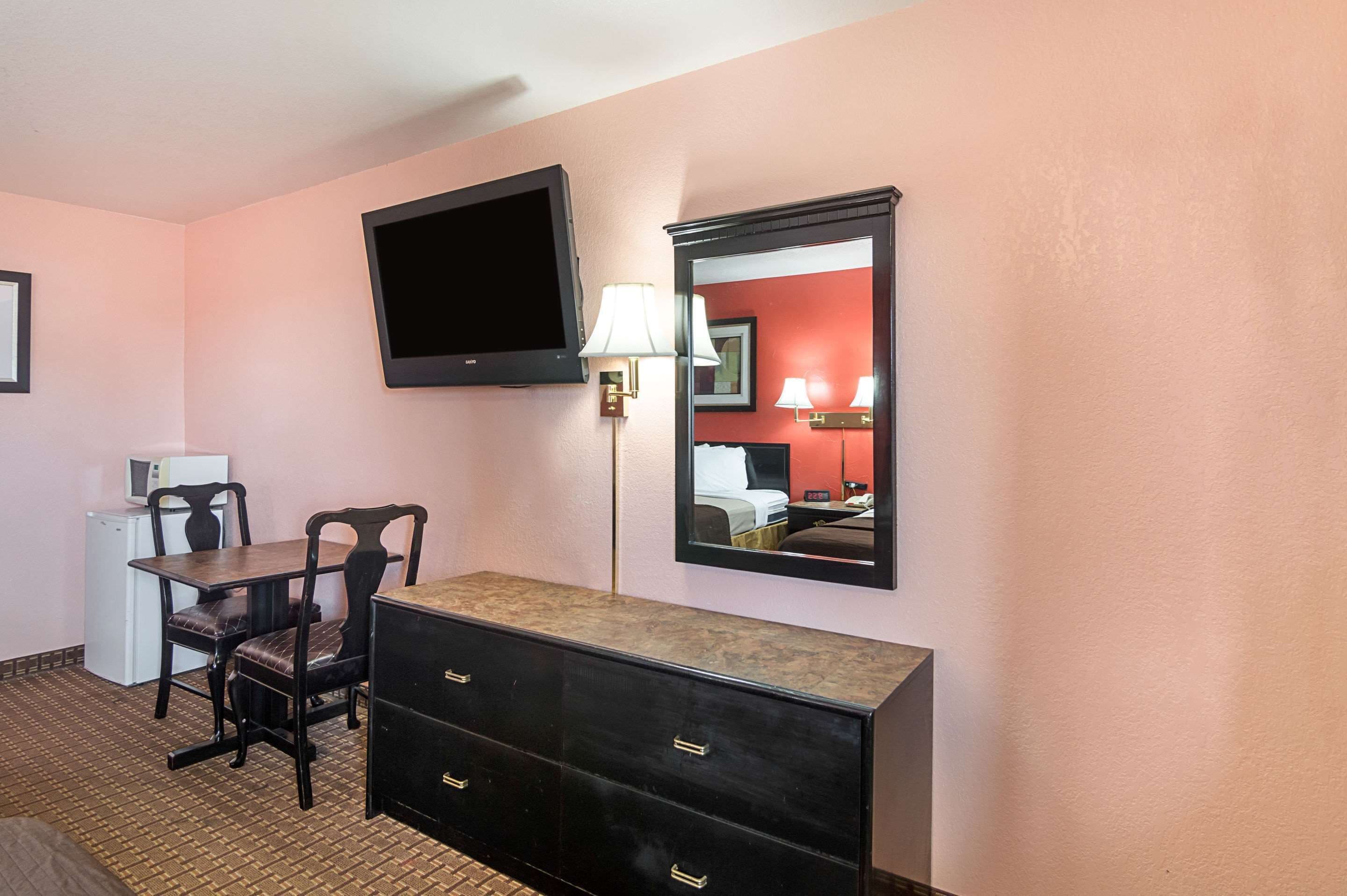 A hotel room with a TV, a desk with a chair, a dresser, a lamp, and a mirror.