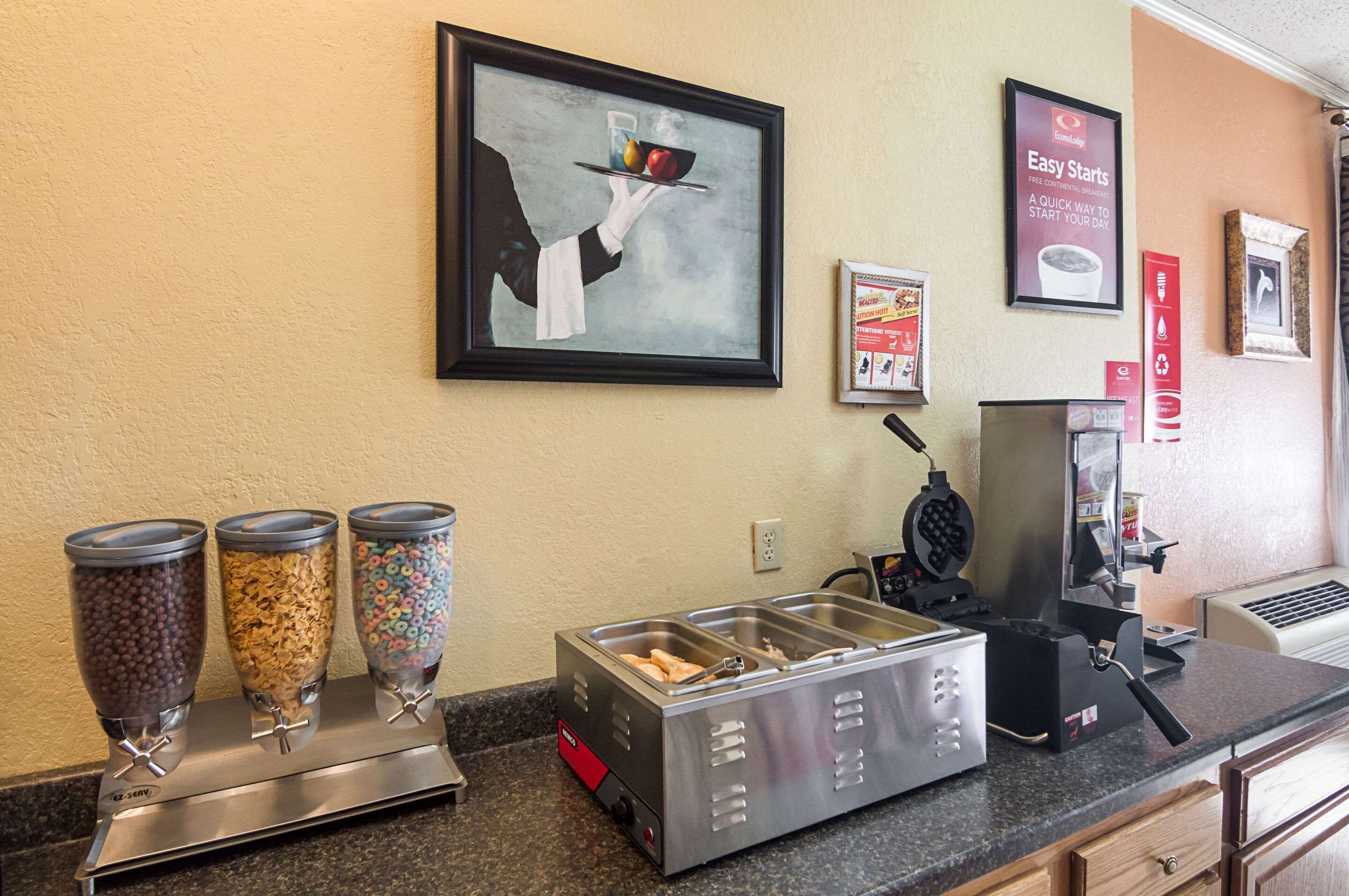 Una barra de desayuno con dispensadores de cereales, una máquina para hacer gofres y una cafetera.