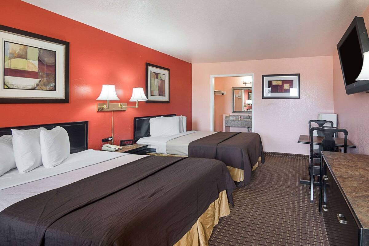 A hotel room with two beds, a desk with a chair, a TV, and artwork on the walls.