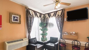A room with a ceiling fan, a large TV, two chairs, a small table, and a potted plant.