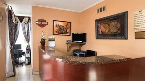 A hotel reception area with a wooden reception desk, a television, and a framed picture on the wall.