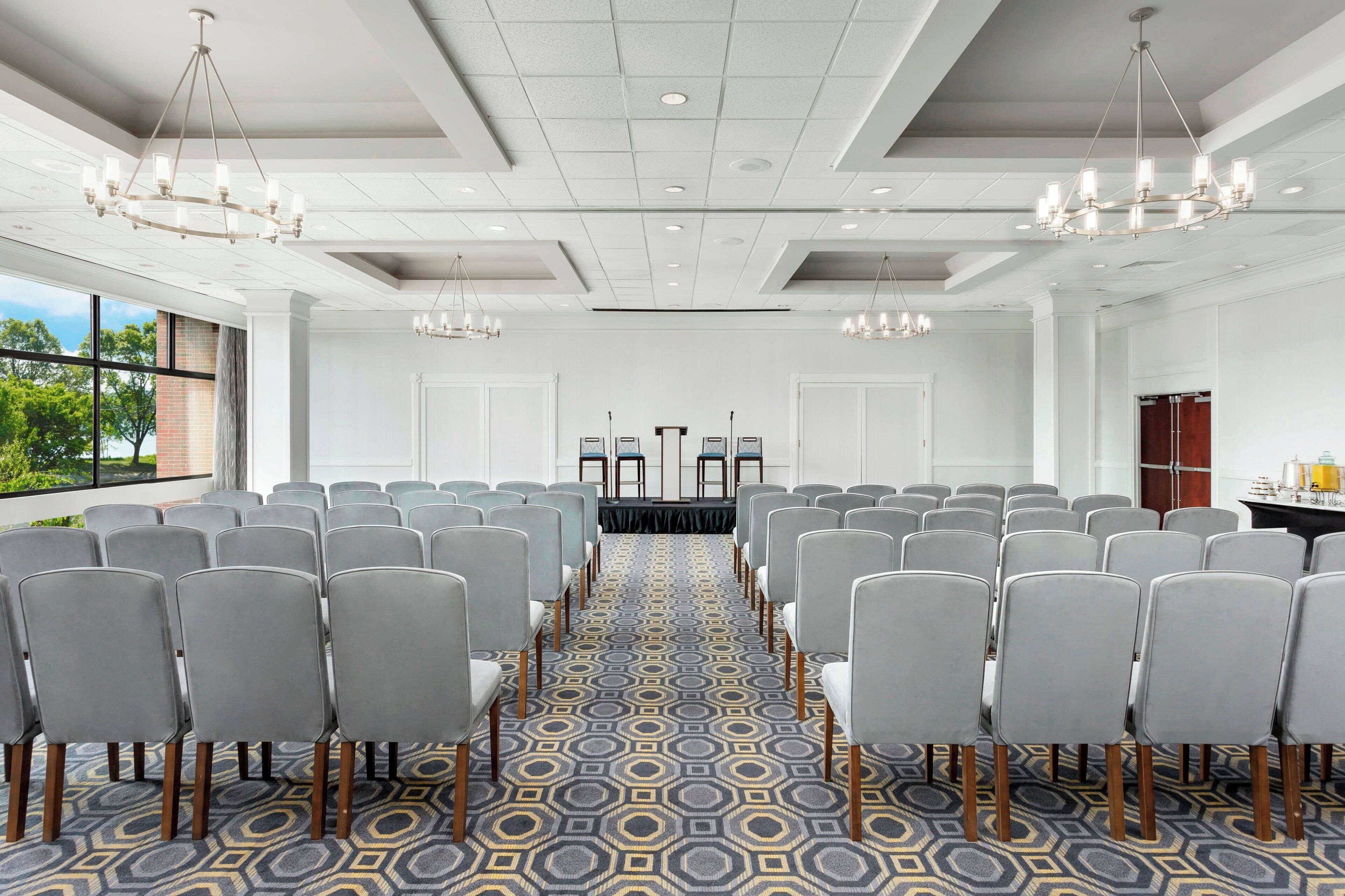 Une salle de conférence avec des rangées de chaises grises, une moquette à motifs et des lustres.