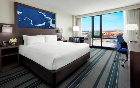 A hotel room with a large bed, a desk, a chair, and a view of the city.