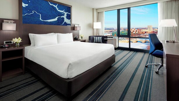 A hotel room with a large bed, a desk, a chair, and a view of the city.