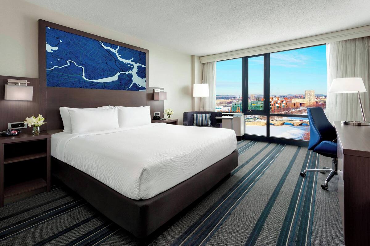 Quarto de hotel com uma cama grande, uma escrivaninha, uma cadeira e vista para a cidade.
