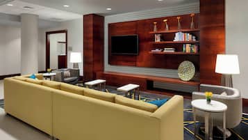 A hotel lobby with a yellow sofa, a flat-screen TV, a bookshelf, and a fireplace.