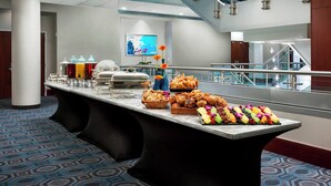 A buffet setup with various food items and a large screen in the background.