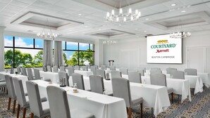 A conference room with multiple tables, chairs, and a large screen displaying Courtyard Marriott Boston Cambridge.