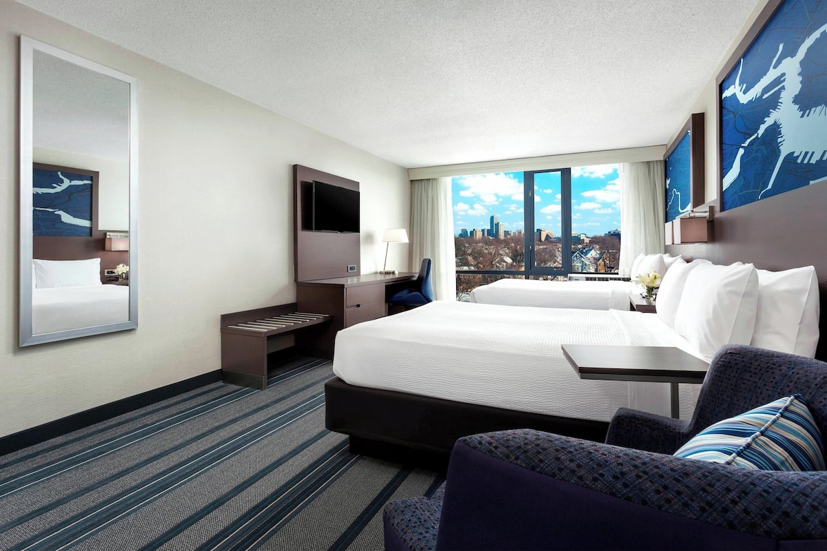 Quarto de hotel com uma cama grande, uma mesa, uma cadeira, uma televisão e vista para a cidade.