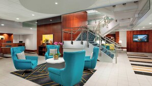 A modern lobby with teal chairs, a reception desk, a staircase, and a TV screen.