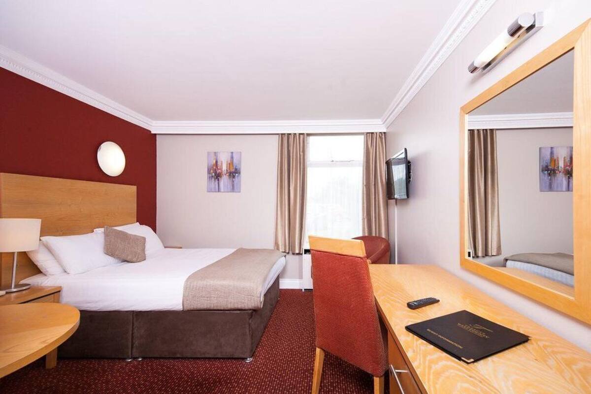 Een hotelkamer met een bed, een bureau met stoel, een televisie en een grote spiegel.