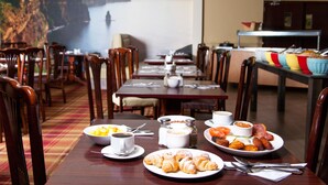 Uma sala de jantar com mesas preparadas para o pequeno-almoço, incluindo croissants, ovos e café.