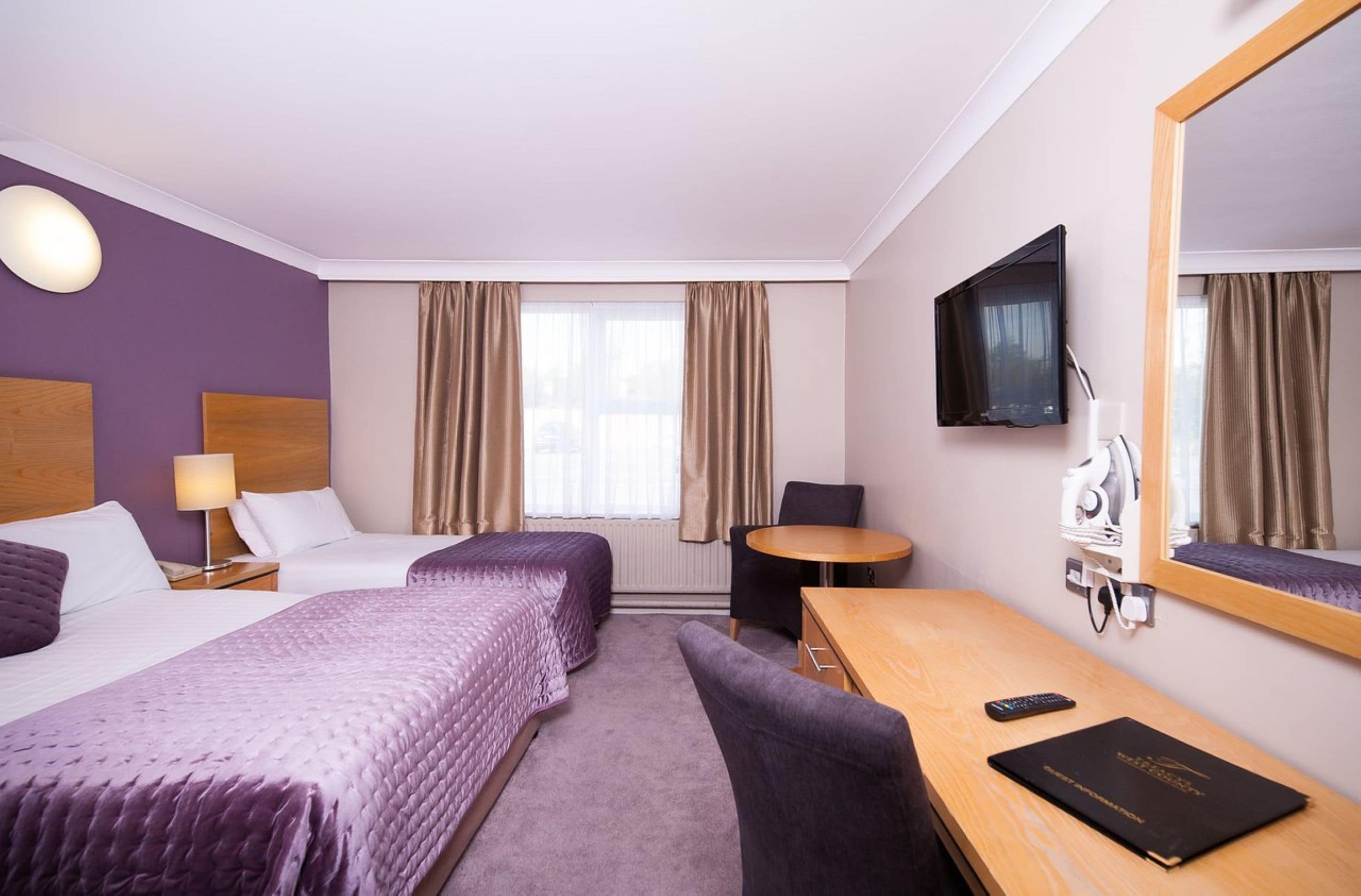 Ett hotellrum med två sängar, ett skrivbord, en stol, en TV och en spegel.