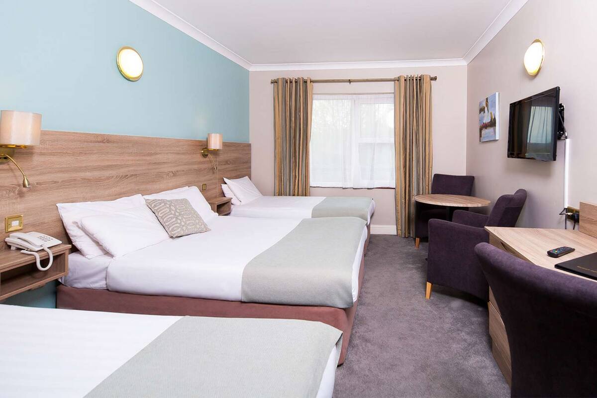 Een hotelkamer met twee bedden, een bureau, een stoel, een televisie en een raam met gordijnen.