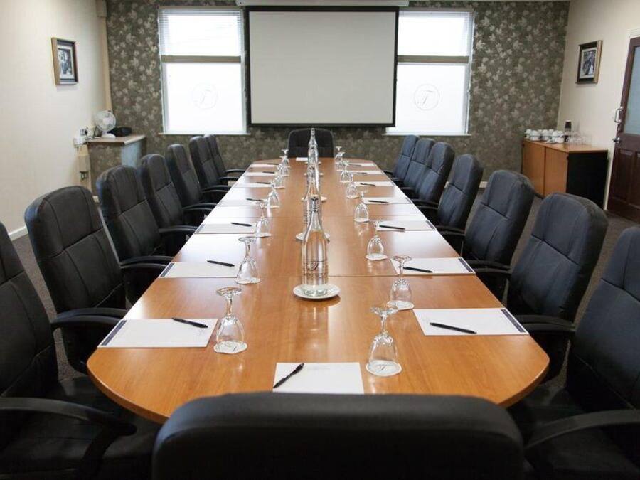 A conference room with a long table, black chairs, and a projector screen.