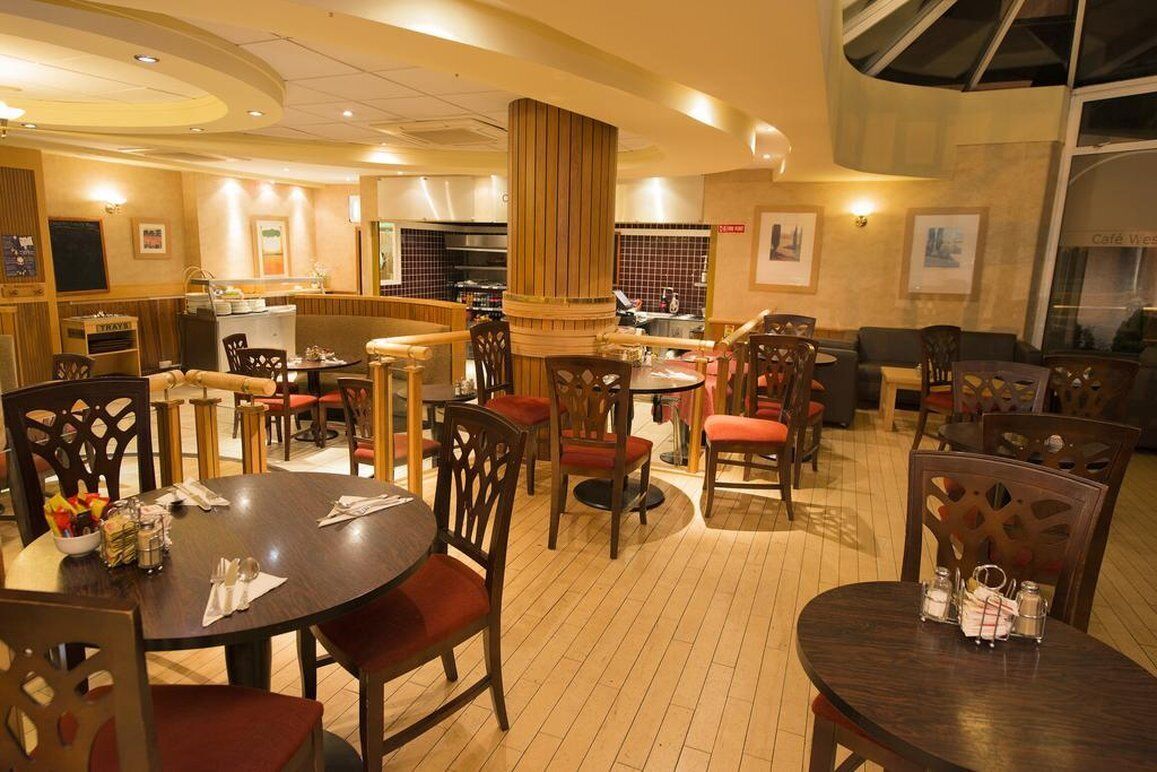 En restaurant med runde borde og træstole, et barområde og et køkken i baggrunden.
